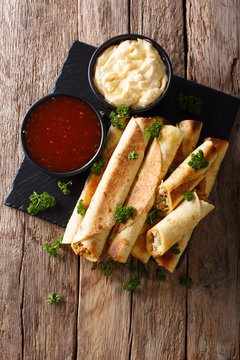 Mexican taquitos with chicken and cheese stuffing close-up, and sauces. Vertical top view
