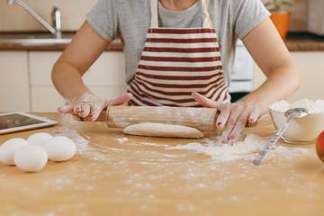 A young beautiful happy woman sitting at a table with flour and tablet, rolling a dough with a rolling pin and going to prepare a Christmas cakes in the kitchen. Cooking home. Prepare food close up.