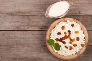 Cottage cheese in bowl with sour cream and raisins on old wooden background with copy space for your text. Top view