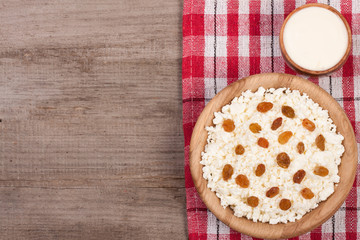 Cottage cheese in bowl with sour cream and raisins on old wooden background with copy space for your text. Top view