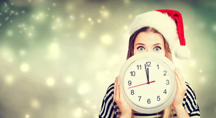 Young woman wearing Santa hat holding a clock showing nearly 12