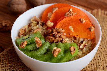 Oatmeal porridge with fruits and nuts toppings. Oatmeal with fresh persimmon, kiwi fruit and walnuts in a round white bowl. Wholesome porridge for Breakfast. Closeup
