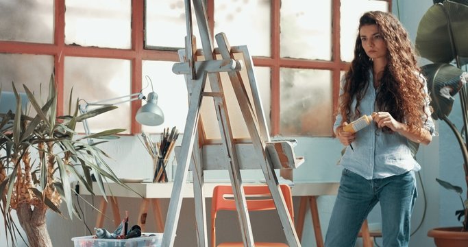 Portrait of a beautiful long-haired female artist at work at her canvas in a studio