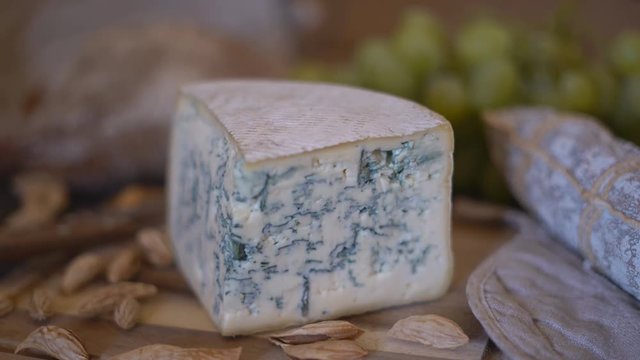 appetizing sausage loaf in a bag of marble fabric. the sausage rests on a wooden table of brown color. In the background a baguette, cheese with green mold and a large bunch of white grapes with a