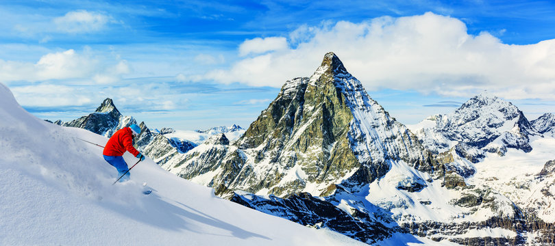 Man skiing on fresh powder snow with Matterhorn in background, Zermatt in Swiss Alps.