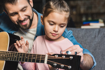 father learning daughter to play guitar