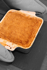 Hot apple crumble being put on slate mat by a person wearing oven gloves