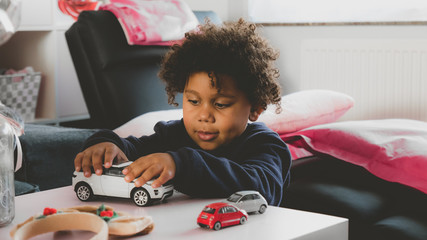 African American kid playing with toy car at home - obrazy, fototapety, plakaty
