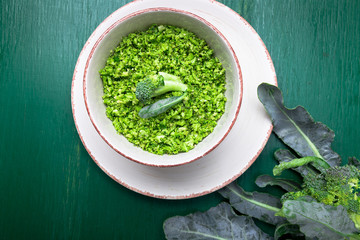 Broccoli rice in bowl on green background. Top view. Overhead. Copy space. Shredded broccoli.