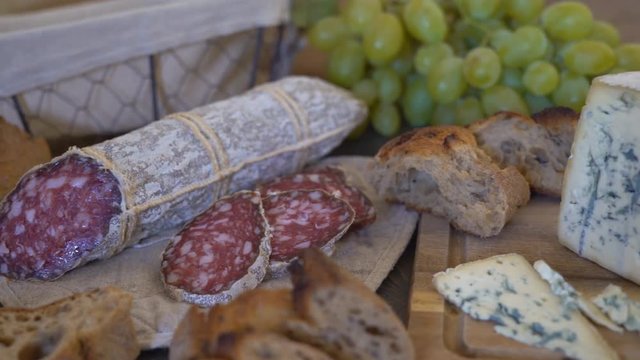 appetizing sausage loaf in a bag of marble fabric. the sausage rests on a wooden table of brown color. In the background a baguette, cheese with green mold and a large bunch of white grapes with a