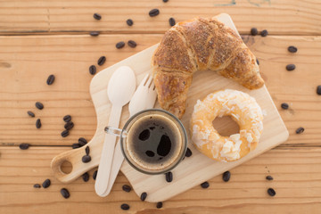 Cup of espresso and croissant on wooden table.