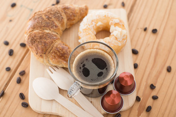 Cup of espresso, espresso capsule and bakery on wooden table.