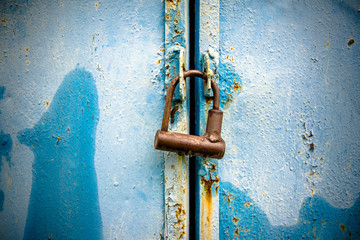     Rusty padlock hanging on a blue metallic background 