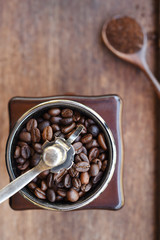 Freshly ground coffee beans in wooden spoon and coffee beans in coffee grinder for background