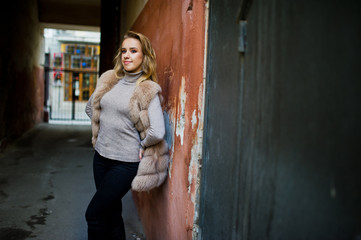 Blonde girl at fur coat posed against old orange wall.