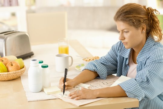 Young woman writing notes in kitchen