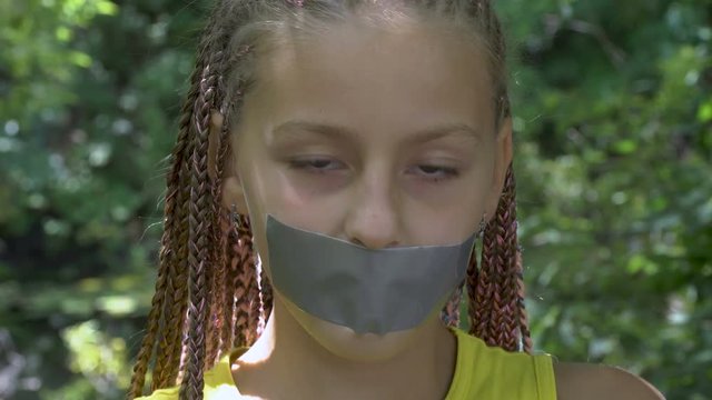 A girl with a taped mouth. Girl looks at the camera (emotion). This video can be used in films about freedom of speech and democracy