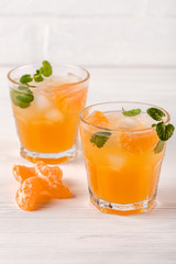 Mandarin cocktail with ice and mint in beautiful glasses and jug, fresh ripe citrus on white wooden background. Sweet orange juice. Close up photography. Selective focus