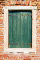 Window with old green wooden shutters in the brick wall solar day, Venice