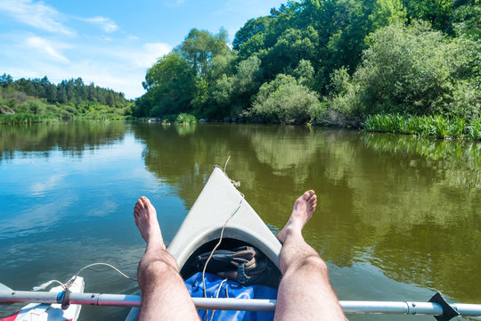 Man relaxing in kayak at the river. Landscape with blue water and green trees