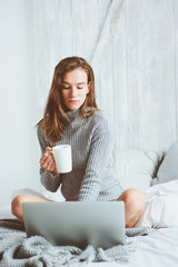 young blogger woman working at home with social media, drinking coffee in early morning in bed. Modern living in scandinavian interior, casual lifestyle