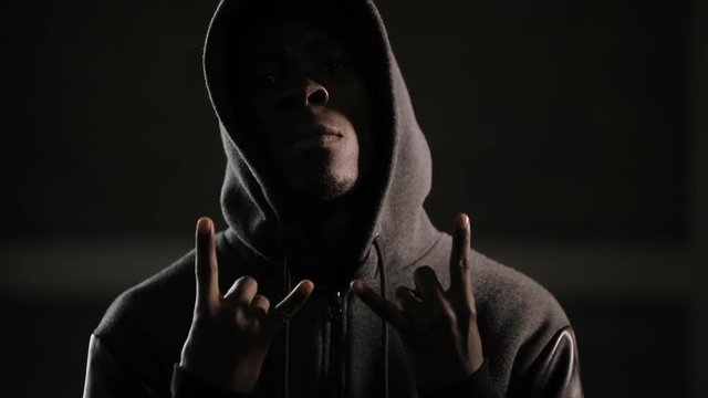 Hooligan man under hood making a rock out gesture in darkness