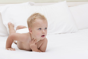 Cute blonde toddler with open mouth in a diaper lying on the white blanket and looking aside. Copy...