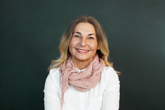 Positive human emotions and feelings. Portrait of beautiful cheerful middle aged woman with loose hair posing at blank studio wall, looking at camera with joyful smile, expressing joy and happiness