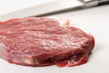 Raw beef steak on the white marble table with chef knife in the background