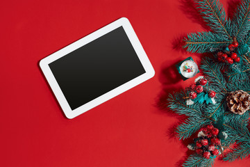 Christmas decorations and white tablet with black screen on hot red background. Christmas and New Year theme. Place for your text, wishes, logo. Mock up.