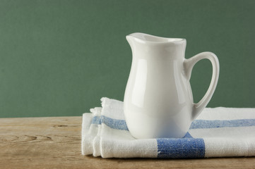 White jug and dishcloth on old wooden table over green background