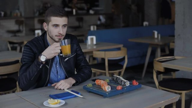 Handsome man eating sushi rolls and drinks juice in cafe 4K.