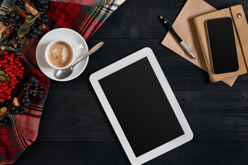 Digital tablet computer with notebook and cup of coffee on old wooden desk. Simple workspace or coffee break with web surfing.