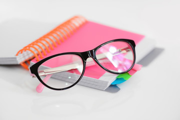 Eye glasses with pink spiral notebook on white background