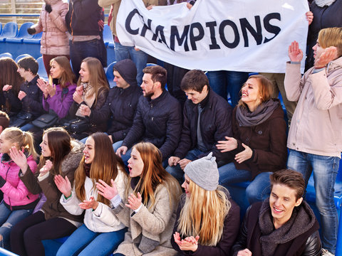 Fans cheering in stadium holding champion banner and singing on tribunes. Large group young people together support your favorite team. Beginning of football match. School competitions.