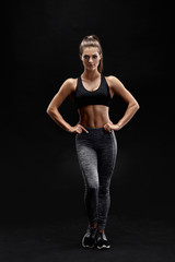 Shot of a strong woman with muscular abdomen in sportswear. Fitness female model posing on black background.