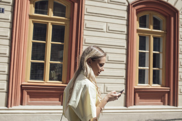 Pretty blonde woman typing on her cell phone and walking.