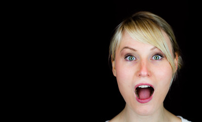 Erstaunte blonde Frau auf schwarzem hintergrund