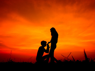 Obraz na płótnie Canvas silhouette of a romantic couple on beauty sunset. A man kneels kissing a girlfriend's hand.
