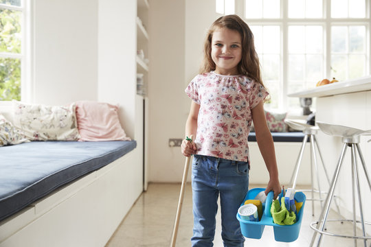 Young girl standing at home with broom and cleaning products