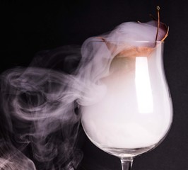 Smoke into cocktail glass on a black background. Witch potion background for Halloween. Unusual bar drink.