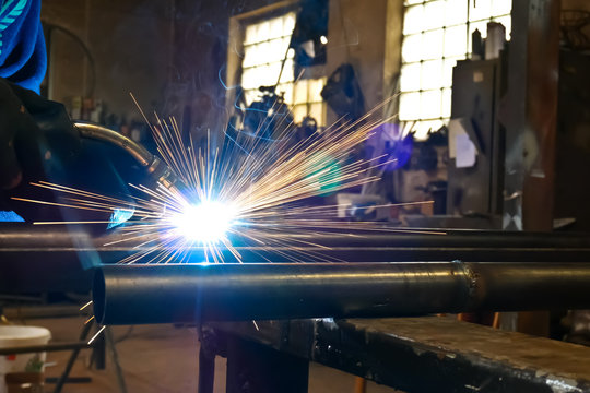 Worker Welds Iron Pipe in the Workroom.