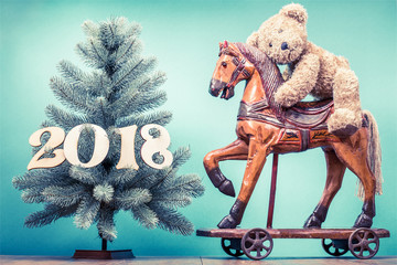 New Year tree with 2018 date and retro Teddy Bear toy riding antique Christmas wooden horse on...