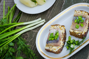Herring, green onions, butter, French mustard and a slice of rye bread on an old wooden table.
