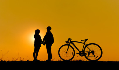 Obraz premium two people holding hands in front of a sunset, with a bicycle to the right.
