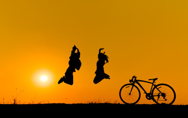 Silhouette of a children jumping on grass with a bicycle.