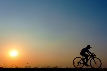 Fototapeta na wymiar silhouette of young woman cyclist on sunset sky with riding along the prairie at yellow evening horizon sea yellow sunset heaven background outdoor