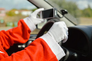 Santa Claus driving car and using mobile smartphone abstract natural outdoors background. Closeup on person hands holding wheel. Festive busy joyful time, modern communication delivery GPS technology.