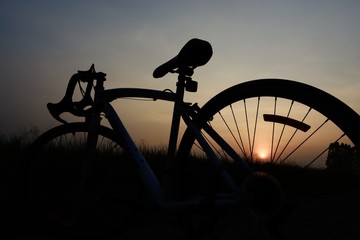a silhouette of a bicycle against a sunset. The sun is setting behind the bicycle and the sky is a...