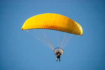 Yellow paramotor wing up in the sky.